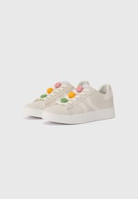 Light beige sneakers with a smooth leather-like finish, featuring pastel rubber floral embellishments on the laces and a white sole.
