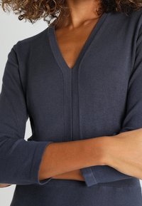 Pull en V bleu marine à coupe ajustée, manches trois-quarts et motif côtelé texturé le long de l'encolure et de l'ourlet.