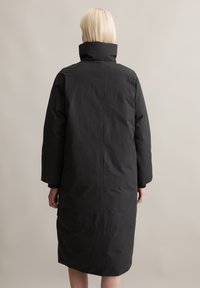 Schwarzer, knielanger Mantel mit hohem Kragen und langen Ärmeln. Hat eine lockere Passform und eine glatte, matte Textur. Keine sichtbaren Verschlüsse oder Muster.