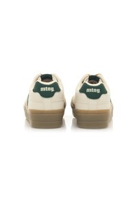 Zapatillas color crema con un acento verde en el talón. Presentan una suela de goma texturizada y detalles de costura. Logo de la marca en la parte posterior.