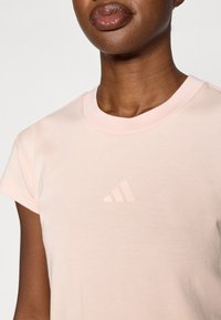 Ροζ βαμβακερό t-shirt με κοντά μανίκια, που διαθέτει μικρό ομοιόχρωμο λογότυπο Adidas στο στήθος και ριμπ λαιμόκοψη. Απαλή υφή.