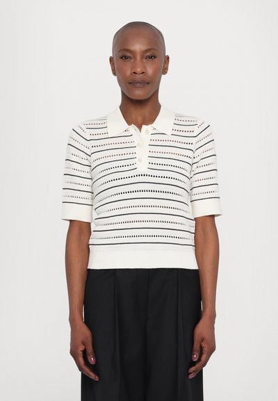 Polo en tricot blanc avec des rayures noires horizontales et des motifs ajourés. Manches courtes et col côtelé avec trois boutons.