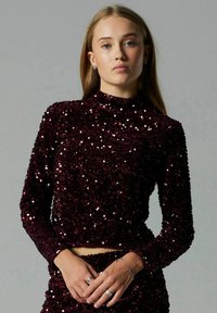 Bordeauxrode top met pailletten, een hoge hals en lange mouwen, met een aansluitend ontwerp en een gestructureerd oppervlak dat licht vangt.