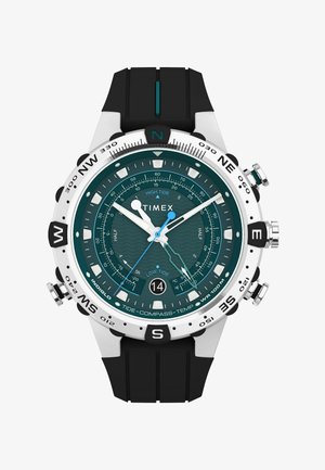 Timex karóra türkiz számlappal, ezüst kerettel és fekete szilikon szíjjal; árapály, iránytű és hőmérséklet funkciókkal rendelkezik.