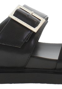 Svart lädersandal med ett brett rem med en rektangulär metallspänne. Skon har en slät yta och en låg, platt sula.