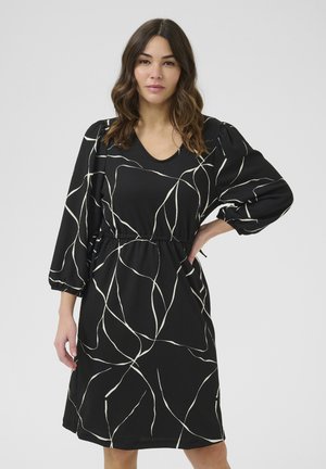 Robe noire avec des manches flottantes et une taille cintrée, arborant un motif abstrait blanc sur un tissu texturé. Design en V.