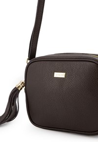 Brown textured leather crossbody bag with a gold-tone logo plate and a tassel detail on the zipper pull. Square shape with a detachable strap.
