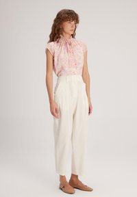 Blusa a fantasia floreale color rosa chiaro con collo arricciato, abbinata a pantaloni bianchi a vita alta e scarpe flat color cammello. Tessuto morbido.