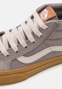 Grå suedes høye sneakers med hvite lærdetaljer. Har hvite snører og en brun gummisåle. Logo-tag i oransje ved ankelen.