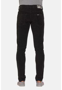 Jeans neri con una vestibilità slim, realizzati in denim. Presentano due tasche posteriori e un'etichetta nera sulla vita. Scarpe grigie visibili.