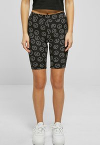 Fekete kerékpáros sort, rugalmas anyagból, szürke színű ismételt békeszimbólum mintával. Fekete cropped top-pal és fehér sportcipővel viselve.