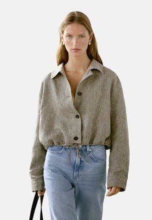 Lys grå, struktureret cropped jakke med krave, knaplukning foran og snoretræk i kanten, båret over lyseblå jeans.