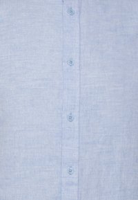 Camisa abotonada de lino azul claro con un acabado texturizado, que presenta pequeños botones azul claro en la parte delantera y un diseño limpio y simple.