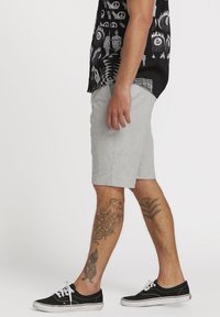 Gray fabric shorts with a straight cut, side pockets, and hemmed edges, paired with black canvas sneakers featuring white laces and sole.