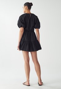 Czarna sukienka z bufiastymi rękawami, z zaznaczoną talią i warstwowym dołem z falbaną, z kluczowym wycięciem na plecach i gładką teksturą.