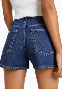 Tmavě modré džínové krátké kalhoty s roztřepeným lemem, vybavené dvěma zadními kapsami a kontrastním šitím. Navrženy s vysokým pasem a přiléhavým střihem.