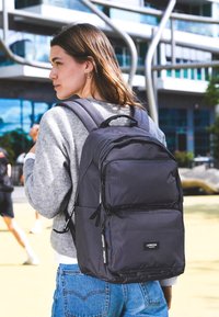 Schwarzer Rucksack mit mehreren Fächern, Reißverschlussverschlüssen und einem strukturierten Stoff. Verfügt über verstellbare Träger und einen oberen Traggriff.
