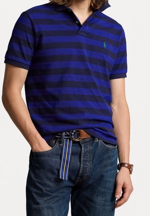 Granatowa i fioletowa koszulka polo w paski z kołnierzykiem, połączona z niebieskimi dżinsami i brązowym paskiem z złotą klamrą oraz paskowymi akcentami.