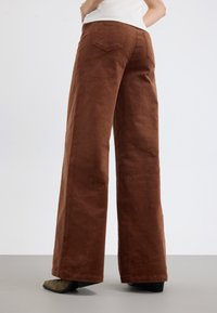 Breda ben corduroybyxor i brunt med en texturerad yta, med bakfickor och en åtsittande midja, parat med mörkgröna skor.