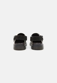Sandale negre din suede cu curele ajustabile, talpă din cauciuc texturat și un design cu spatele deschis, având vârful rotund și un hardware minim.