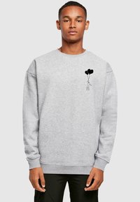 Sudadera gris de tejido suave con un pequeño gráfico negro de una figura sosteniendo tres globos en el lado izquierdo del pecho. Diseño de corte relajado.