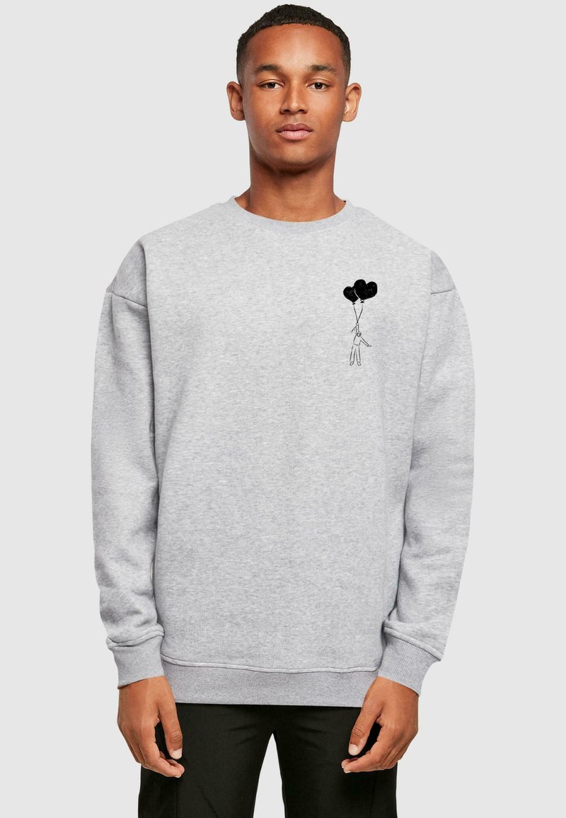 Sudadera gris de tejido suave con un pequeño gráfico negro de una figura sosteniendo tres globos en el lado izquierdo del pecho. Diseño de corte relajado.