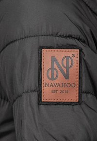 Zwarte pufferjas met een bruine leren logo patch met de tekst "NAVAHOO" en "EST 2014", genaaid op de stof.
