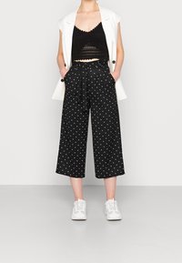 Svarta culottbyxor med vita prickar, med papperspåse midja och sidfickor. Kombineras med en svart crop top och vita sneakers.