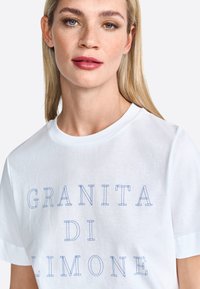 White cotton t-shirt featuring blue outlined text "GRANITA DI LIMONE." Classic crew neckline and short sleeves. Smooth texture.