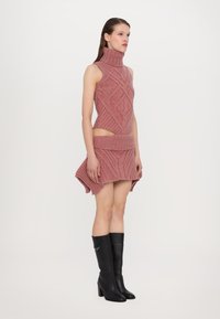Abito in maglia di un rosa chiaro con colletto alto, caratterizzato da un motivo a rombi e sezioni ritagliate; abbinato a stivali neri con tacco al ginocchio.