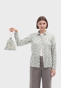 Camisa de botones con un patrón botánico en verde y blanco; tela suave, mangas largas. Acompañada de una pequeña bolsa con cordón y etiqueta.