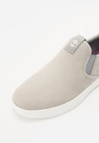 Grå nubuck slip-on sko med rund tå, elastiske sideaksenter og hvit gummisåle. Har en liten logo på hæltappen.