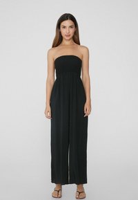 Mono negro sin tirantes con un cuerpo fruncido. Diseño fluido y de pierna ancha, hecho de una tela ligera, con una textura suave y un detalle mínimo.