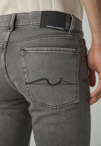 Jeans in denim grigio con una forma aderente, caratterizzati da un design della tasca posteriore e un patch in pelle nera con logo sulla vita.