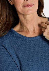 Blauer, strukturierten Strickpullover mit Rundhalsausschnitt und gerippten Abschlüssen. Nahaufnahme zeigt das Muster des Stoffes und die weiche Textur.