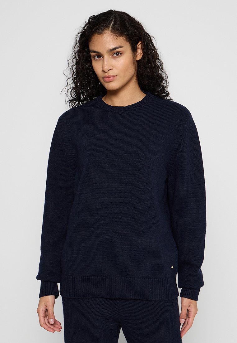 Marineblauer gestrickter Pullover mit gerippten Bündchen und Saum, der einen Rundhalsausschnitt und ein kleines metallisches Logo-Detail am unteren Ende aufweist.