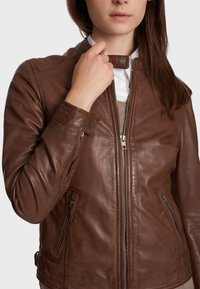 Hnědá kožená bunda se zipem vpředu, vysokým límcem a dvěma zipovými kapsami. Má hladkou texturu a přiléhavý střih.