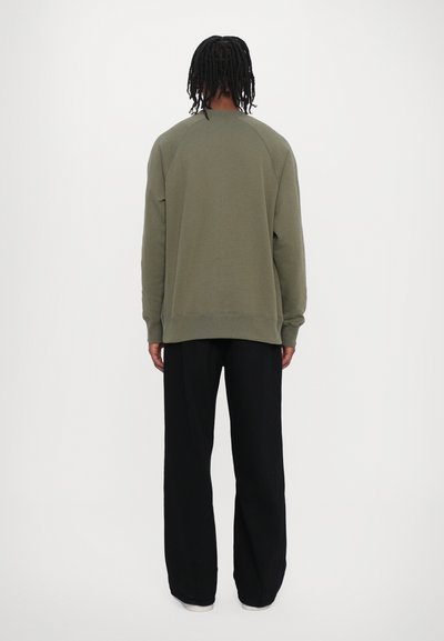 Olivovo zelená mikina s raglánovými rukávmi, s okrúhlym výstrihom a rebrovaným lemom. V kombinácii s čiernymi širokými nohavicami.