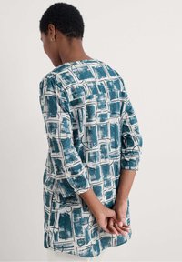 Lichte tuniek met een geometrisch blauw-wit patroon, drie kwart mouwen en een ronde halslijn, gemaakt van een soepele stof.