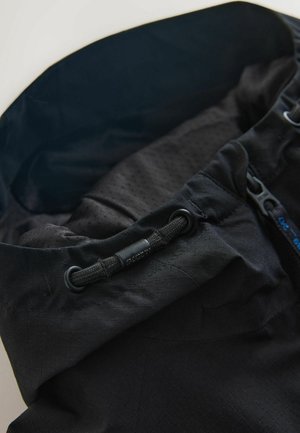 Tissu technique noir avec une surface texturée, doté d'une fermeture à cordon de serrage et de détails de fermeture éclair bleue contrastante.