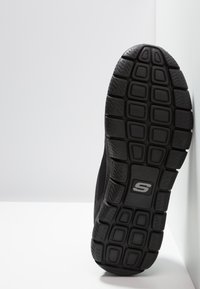 Black athletic shoe sole featuring a textured rubber bottom with rectangular and hexagonal patterns, and a small logo on the side.