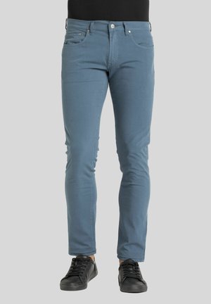 Jeans en denim slim fit de couleur bleu clair, dotés de poches avant, d'une fermeture éclair et de baskets noires pour un look décontracté.