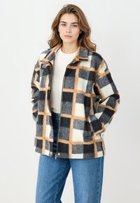 Grijs, crèmekleurig en oranje geruit jack, gemaakt van zachte stof, met een rits aan de voorkant, een kraag en zijzakken, gedragen over een lichte top.