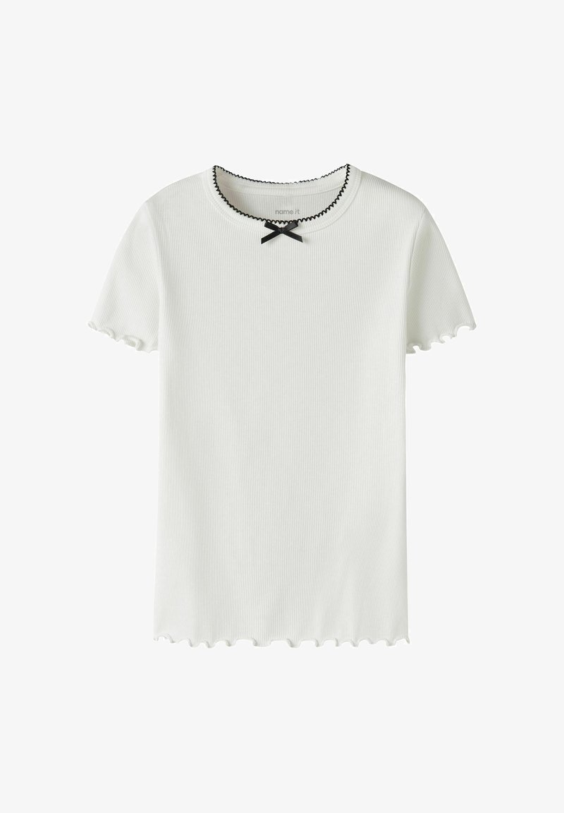 Λευκό ριμπ μπλουζάκι με κοντό μανίκι και μαύρες κυματιστές άκρες στο γιακά, τα μανίκια και το τελείωμα, με ένα μικρό μαύρο φιόγκο στον λαιμό.