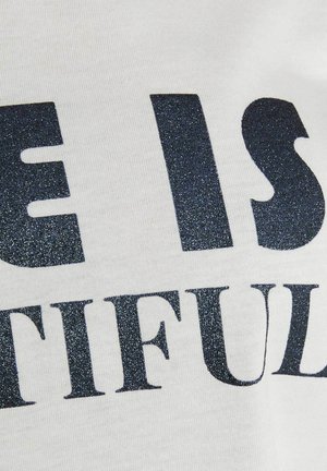 Primo piano di un tessuto bianco con testo nero glitterato che mostra parole parziali "E IS" e "TIFUL" in carattere grassetto.