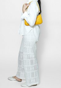 Witte, textuurvolle, kantpatroon brede broek, gecombineerd met een witte overhemden en een kleine gele handtas. Witte instapschoenen maken de look af.