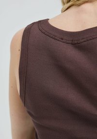 Débardeur côtelé en brun foncé avec un col arrondi et des bretelles larges, présentant une surface texturée. Coutures visibles autour de l'encolure.