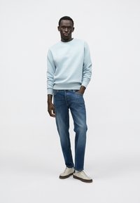 Šviesiai mėlynas džemperis su apvalia iškirpte, džinsai ir smėlio spalvos sportbačiai. Džemperis turi ribinius rankogalius ir apačią, dera kasdieniniam, aptemptam stiliui.