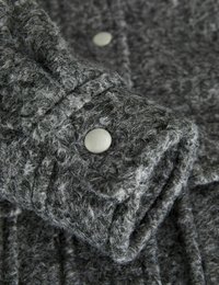 Tessuto grigio con texture e finitura pelosa, con un polsino abbottonato con bottoni grigi chiari e un motivo a coste. Materiale morbido e spesso.