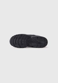 Semelle de chaussure de sport noire avec un design robuste, présentant des motifs de bande de roulement texturés et des blocs surélevés pour une adhérence et une durabilité accrues.